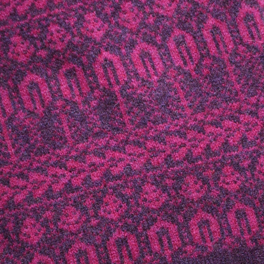 Pink and purple patterned scarf with fringe on a wooden surface.