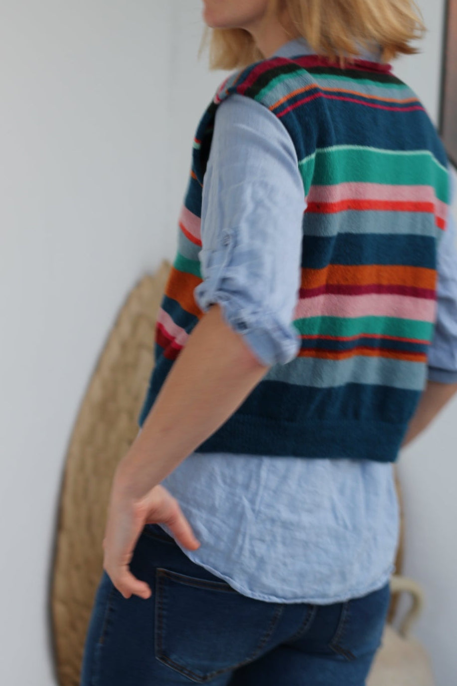 Person wearing a colorful striped sweater and blue jeans on a white background