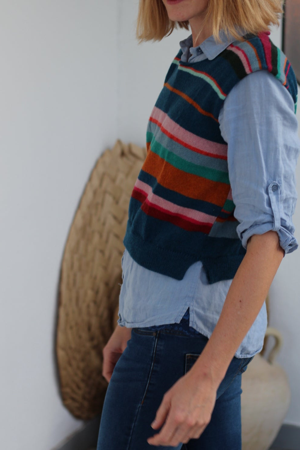Person lying on a white floor wearing a colorful striped sweater and blue jeans.