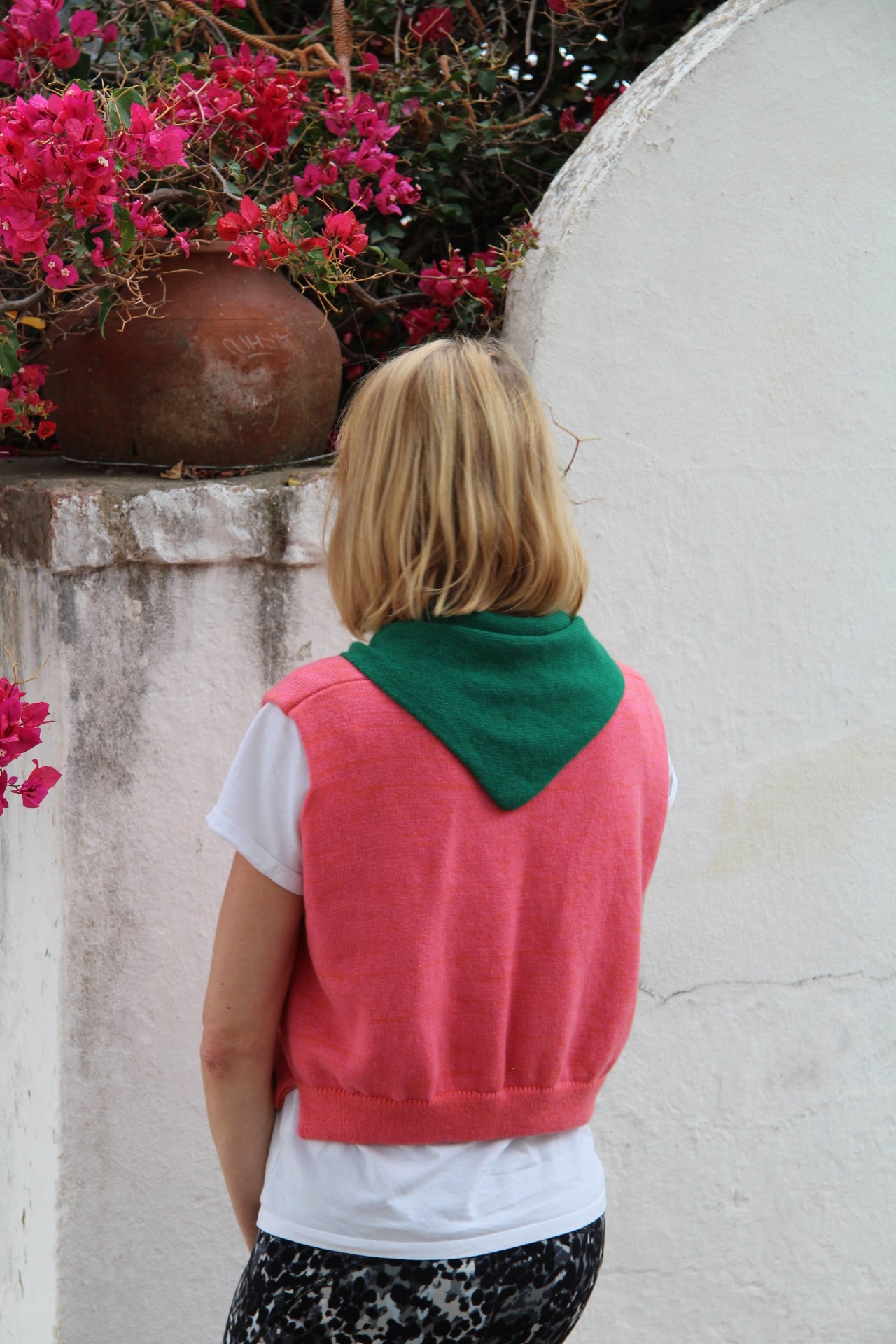 Person wearing a colorful dress with pink and green sections, standing on a stone surface with flowers in the background.