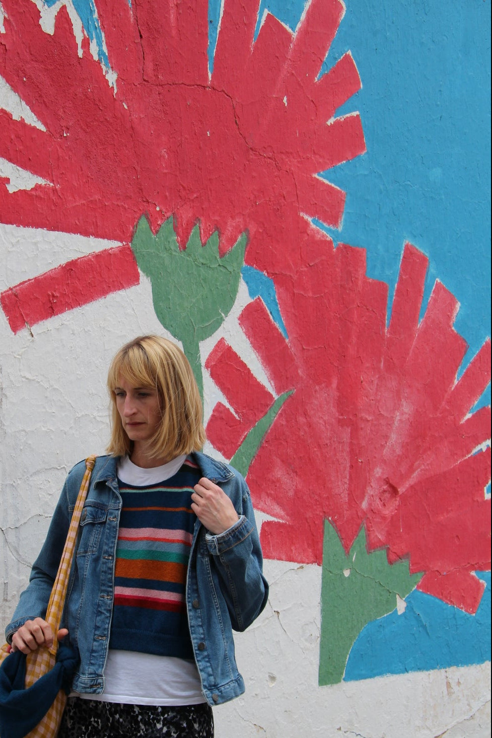 Person standing next to a colorful flower mural on a wall.