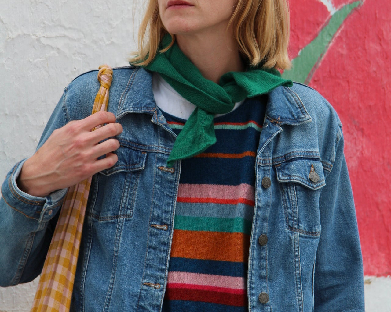 Person wearing a colorful striped shirt and denim jacket against a multicolored abstract background