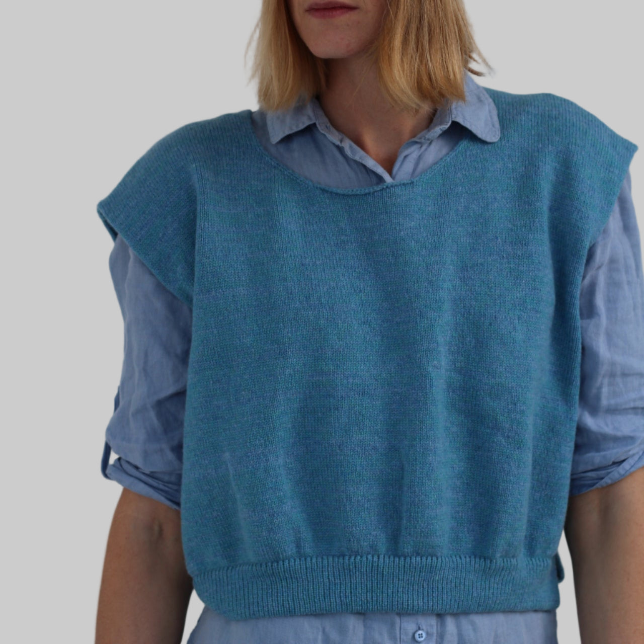Person wearing a blue sweater vest over a shirt with a plain background
