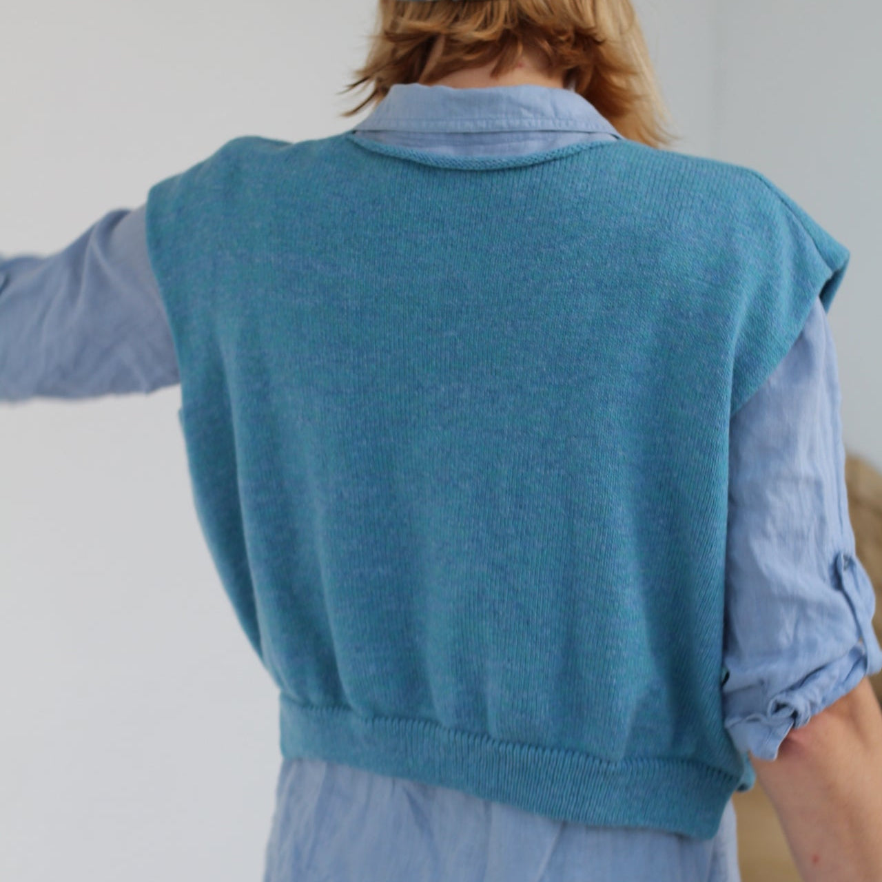 Person wearing a teal sweater over a light blue shirt with a white background