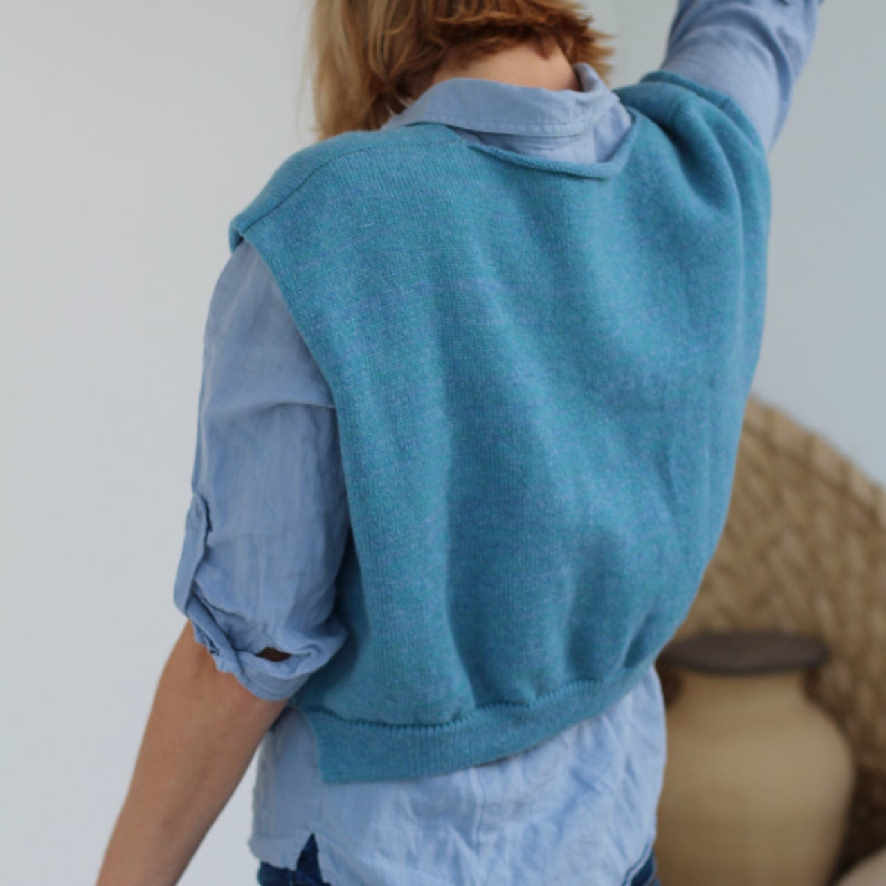 Person wearing a blue sweater over a light blue shirt with jeans, standing on a white background.
