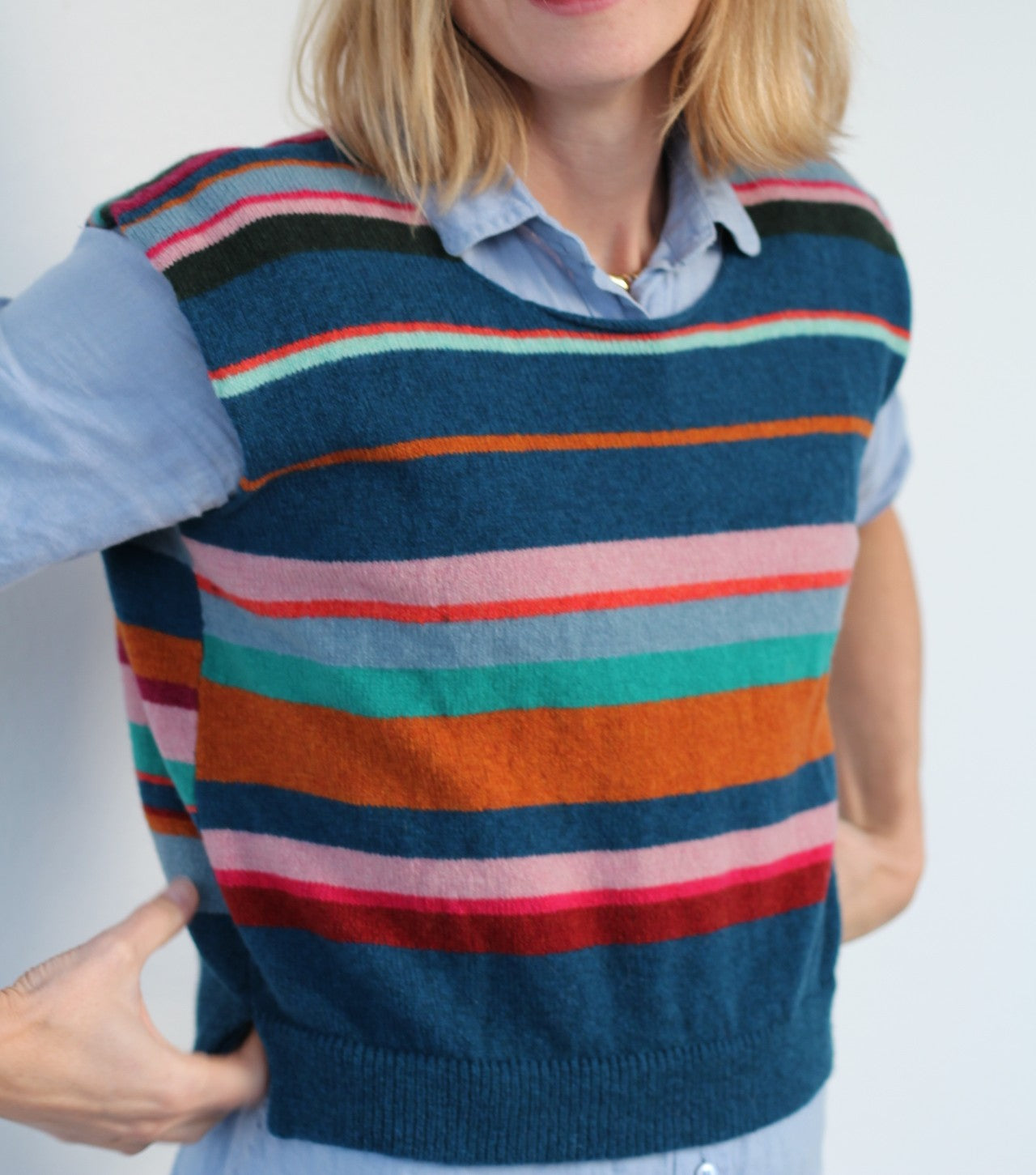Person wearing a colorful striped sweater vest against a plain background