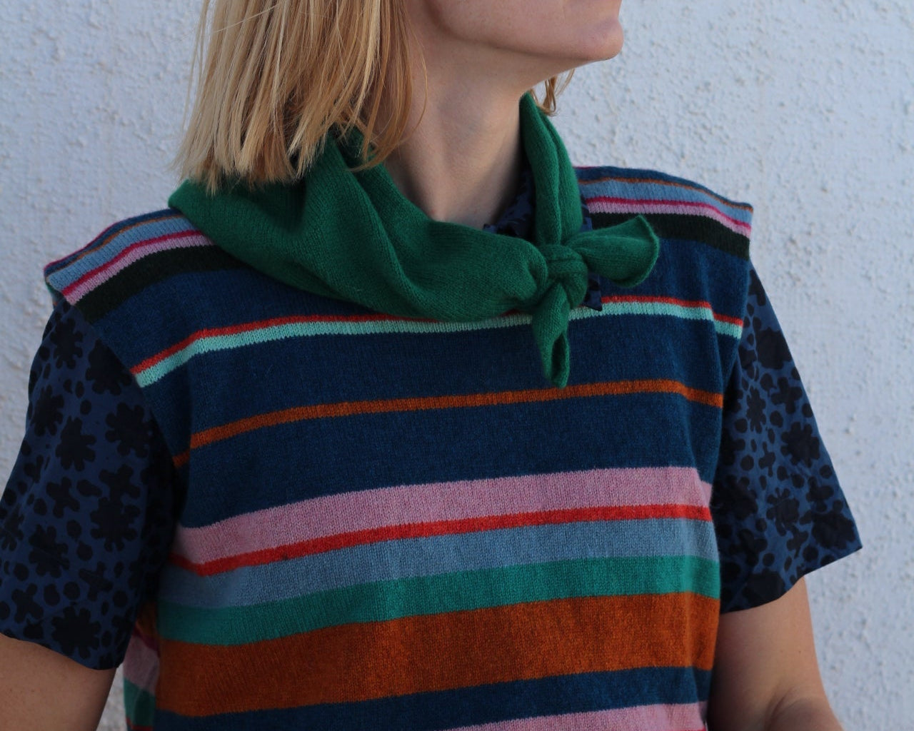 Person wearing a colorful striped sweater with a green bow against a white background