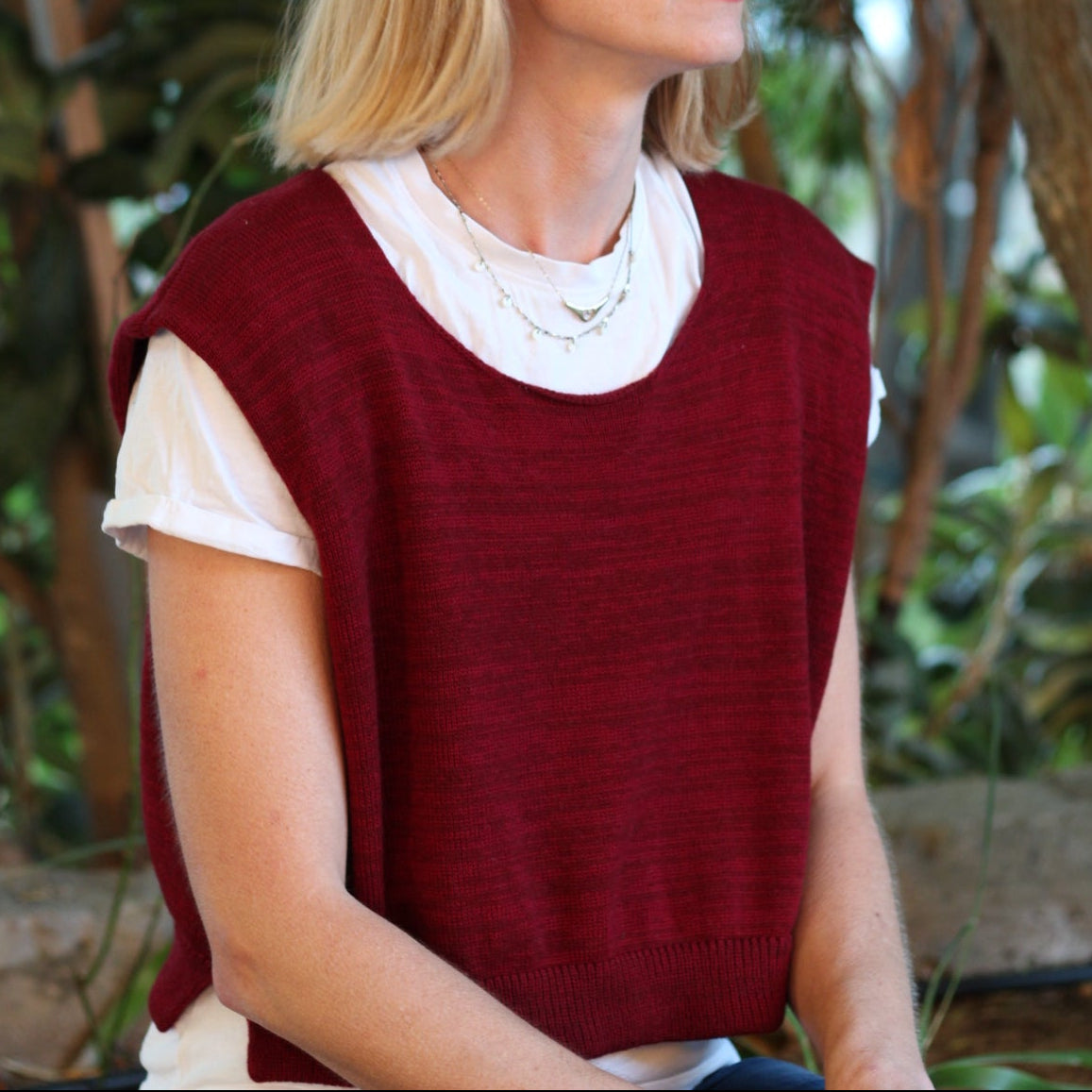 Person wearing a red vest over a white shirt with a blurred natural background