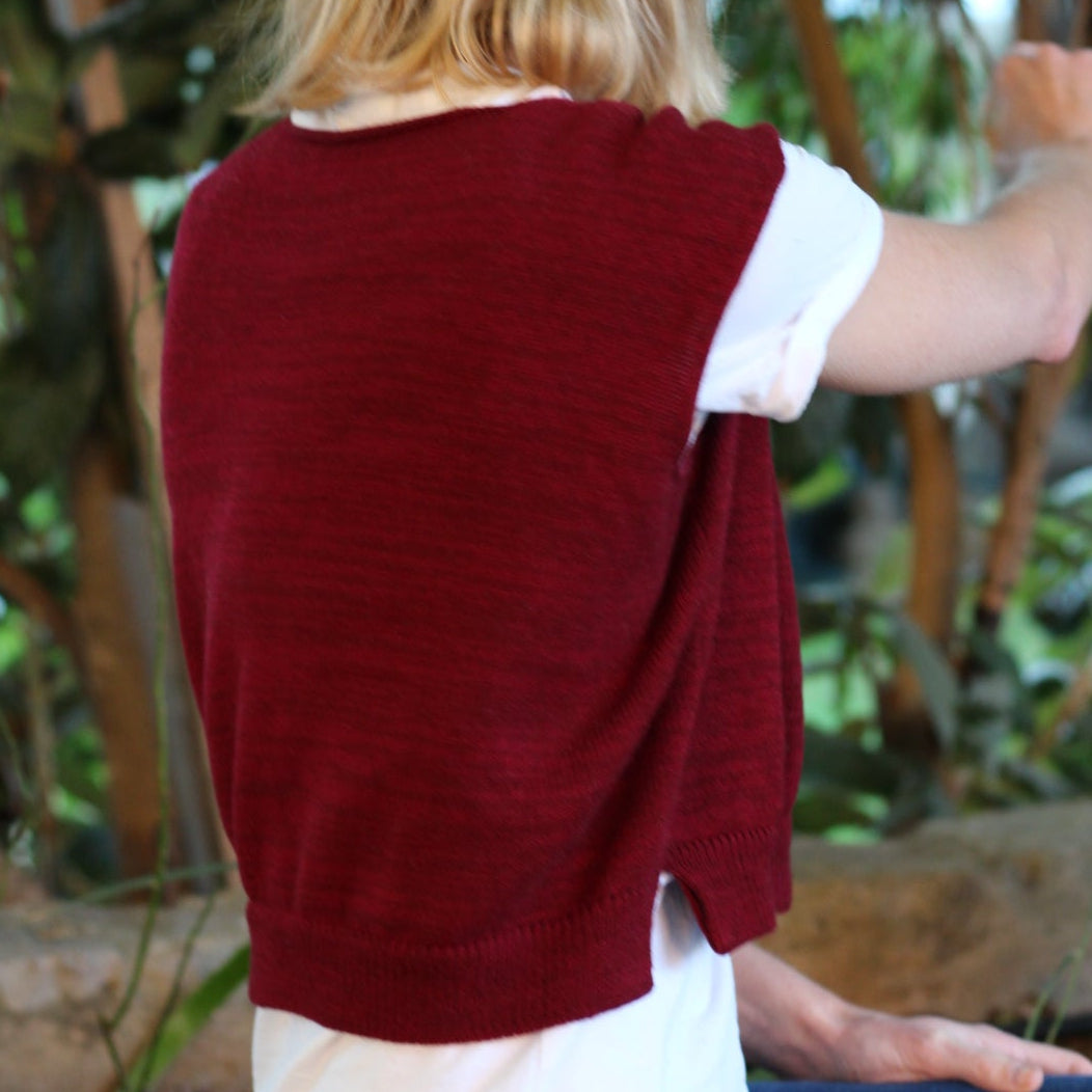 Person wearing a red sweater and white shirt, bending over in a natural setting with trees.