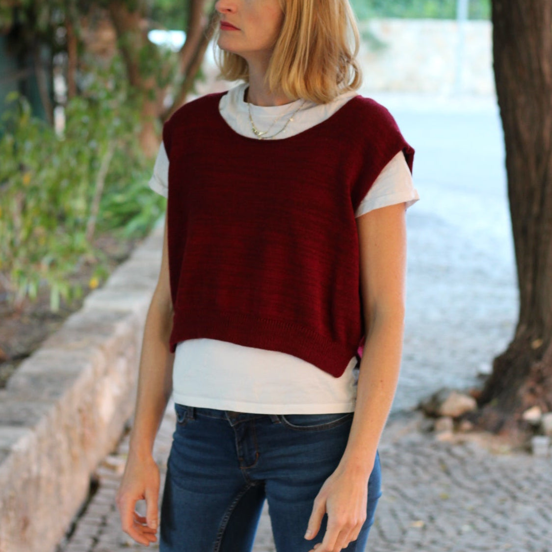 Person wearing a red and white sweater with blue jeans standing outdoors.