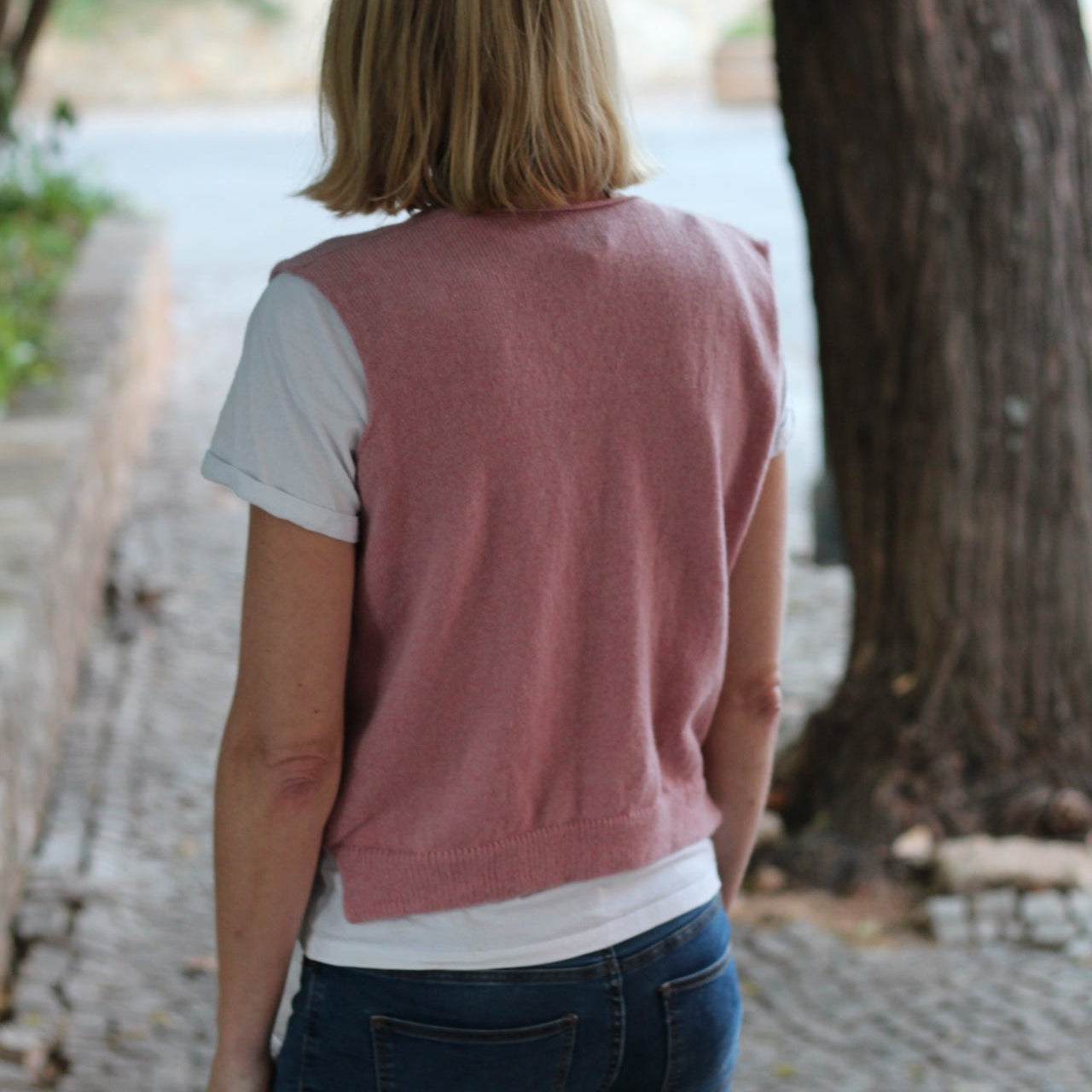 Person wearing a pink sweater and blue jeans standing outdoors with a blurred background