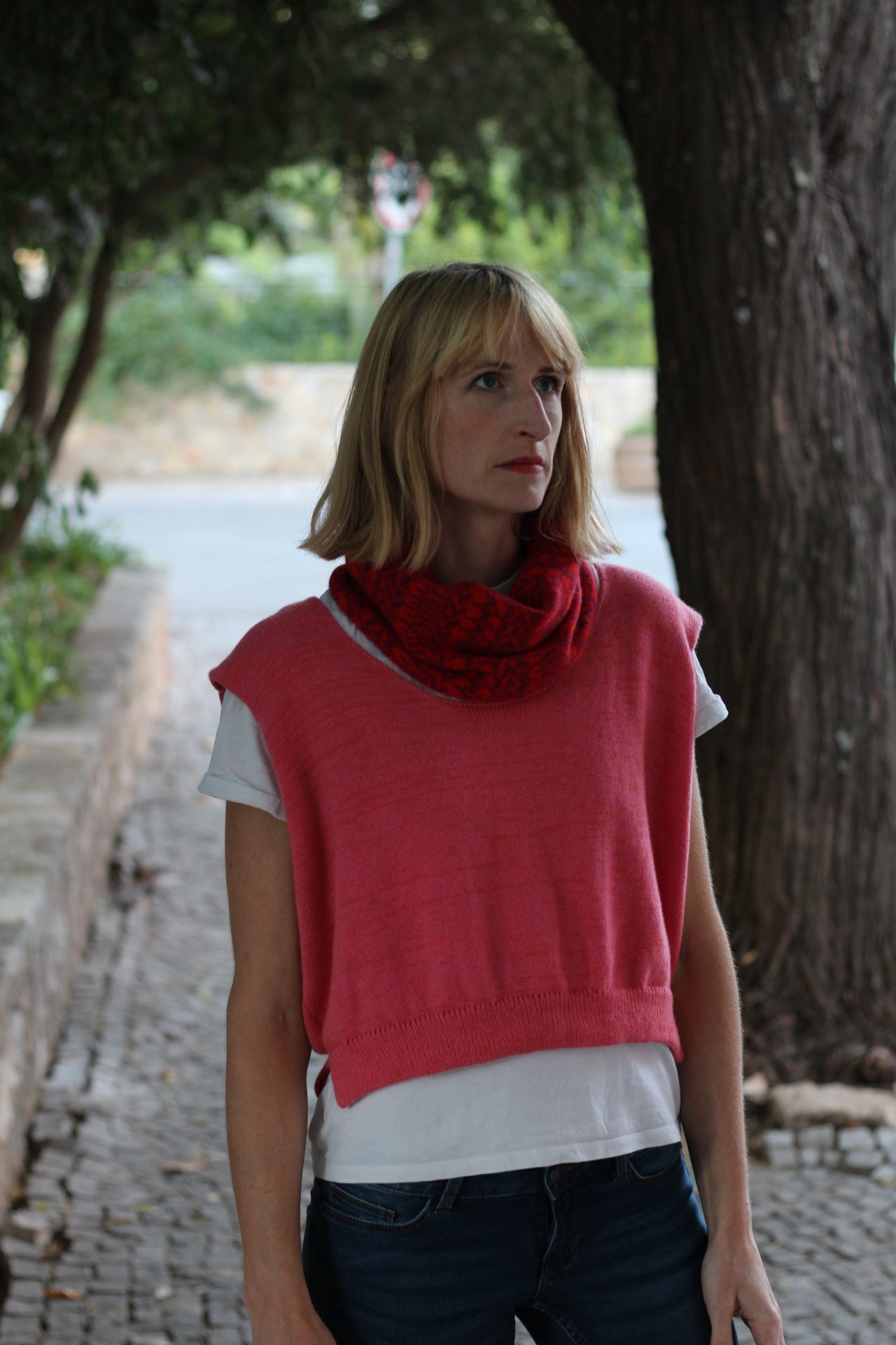 Woman wearing a red sleeveless top with a white shirt underneath, standing outdoors.