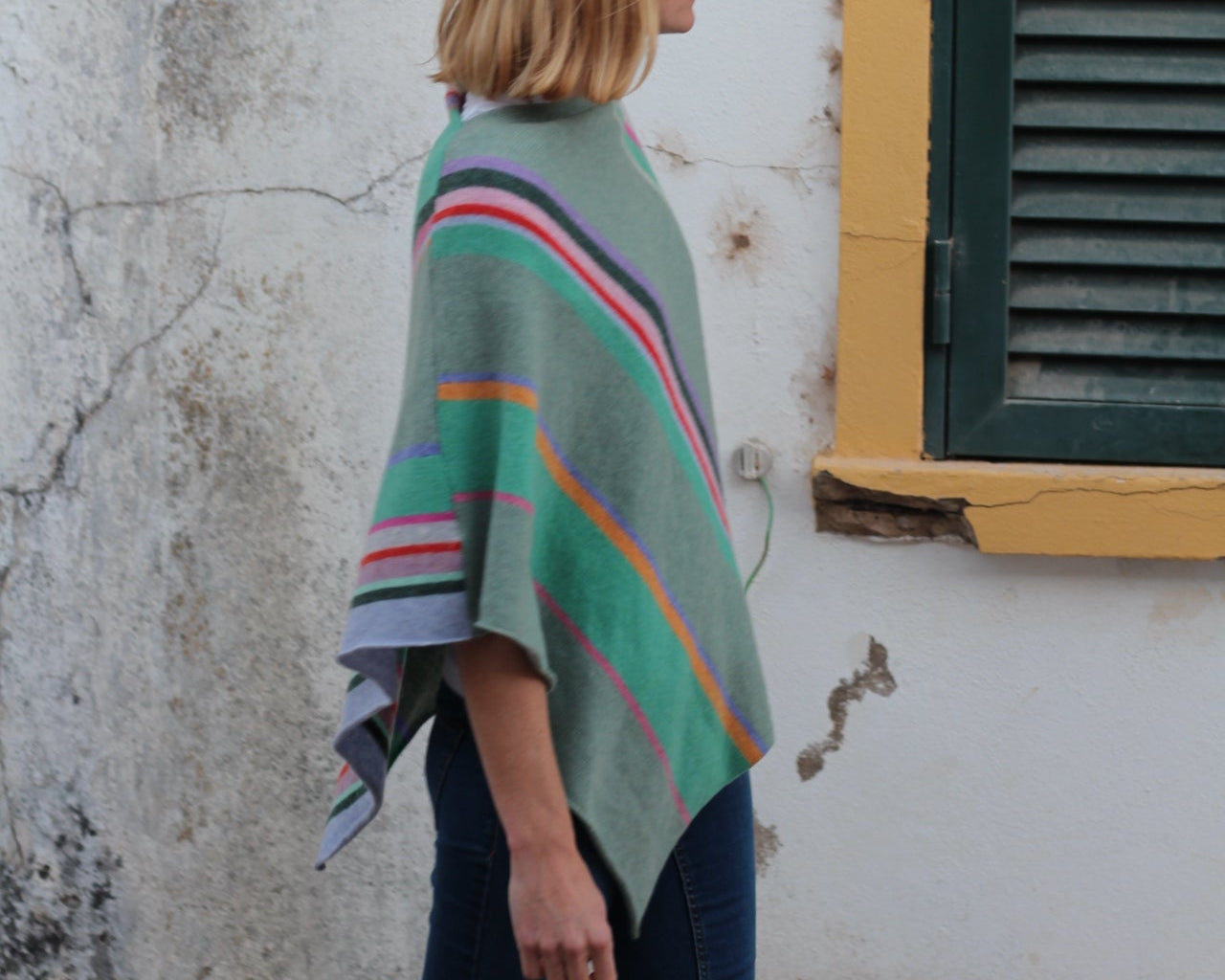 Person wearing a colorful sweater standing next to a yellow wall with a green air vent.