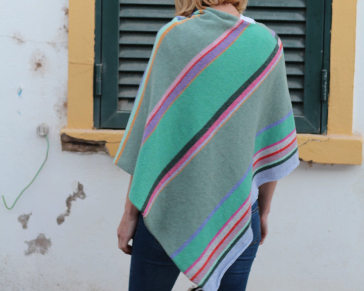 Person wearing a colorful blanket over their shoulders standing in front of a green door.