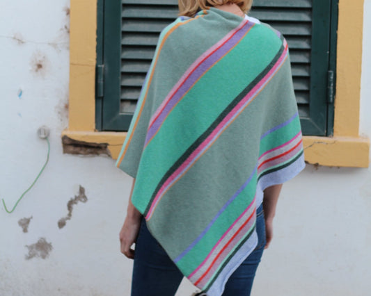 Person wearing a colorful blanket over their shoulders standing in front of a green door.