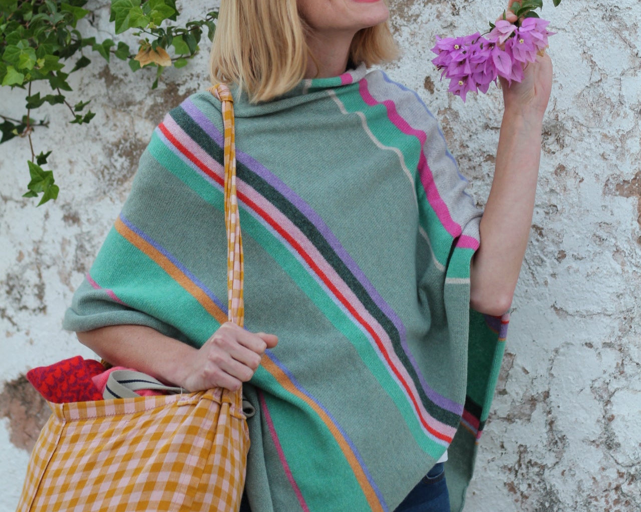 Person lying on a stone surface with a colorful blanket, holding a flower, surrounded by purple flowers.