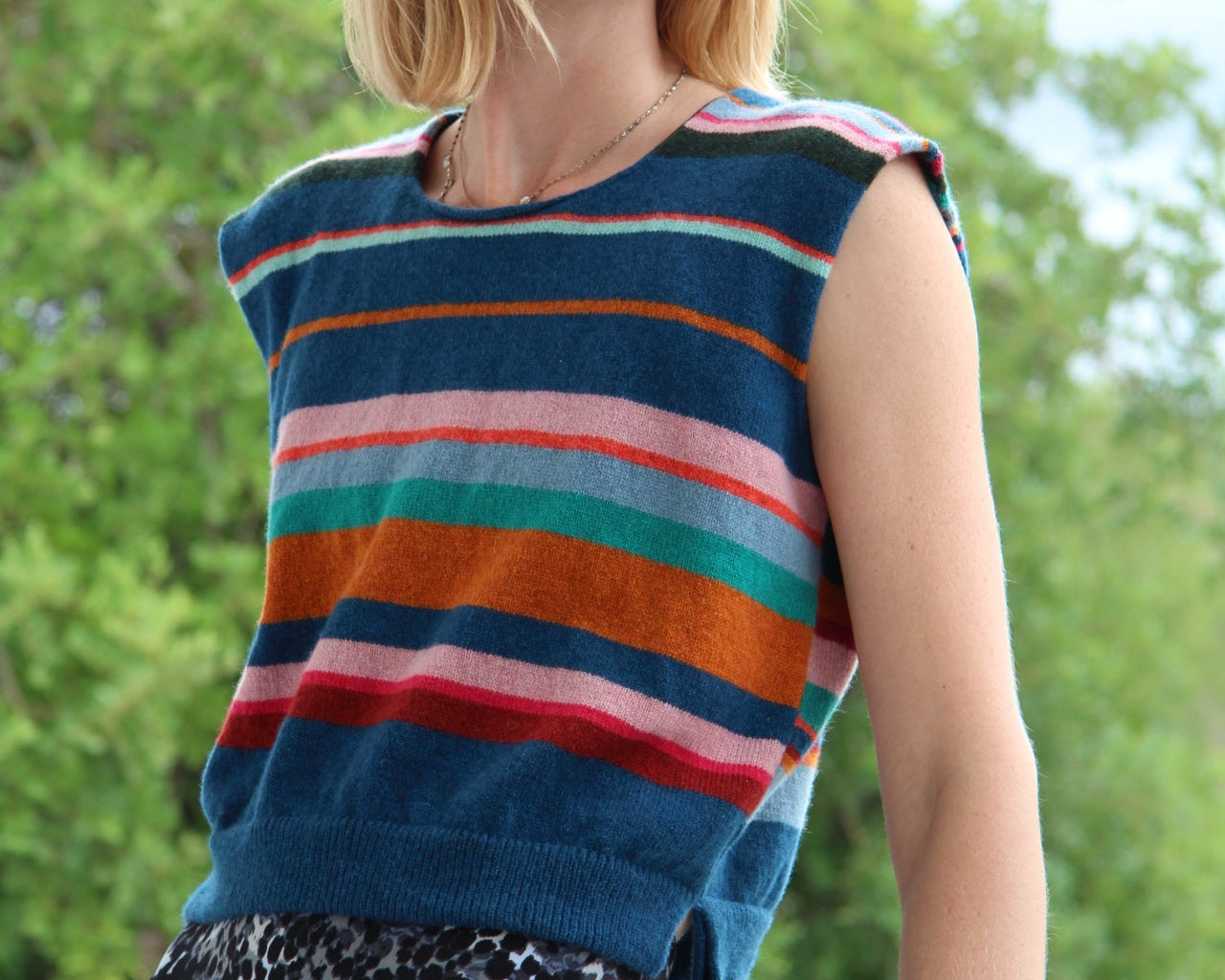 Person wearing a colorful striped sleeveless top with a blurred green background