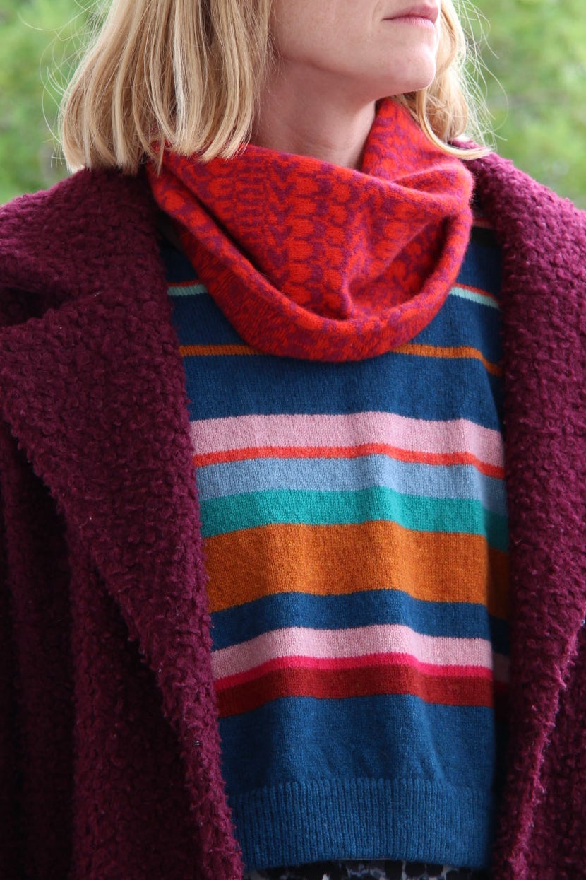 Person wearing a colorful striped sweater with a red cardigan outdoors