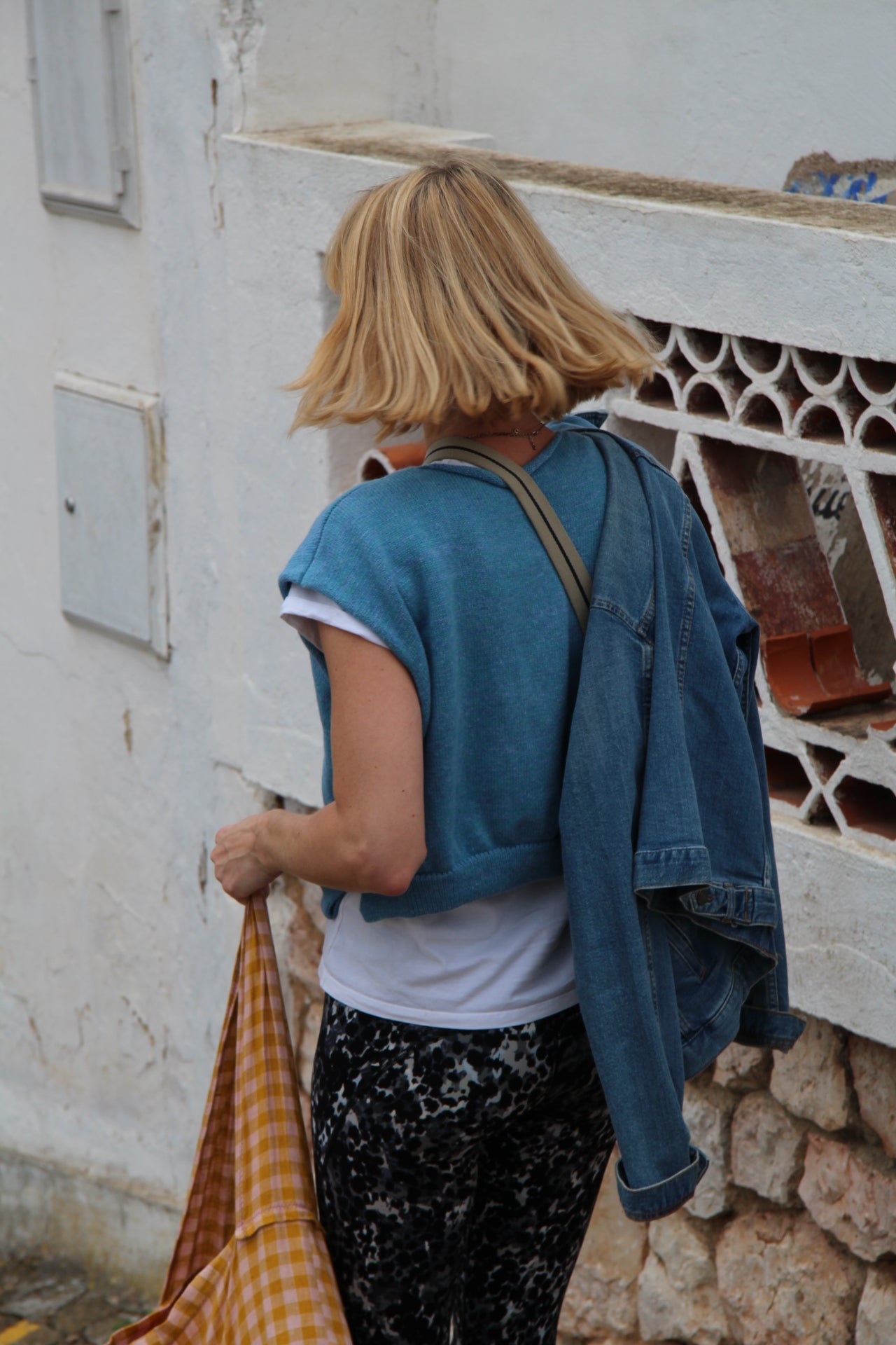 Person with a yellow checkered bag walking on a stone pavement.