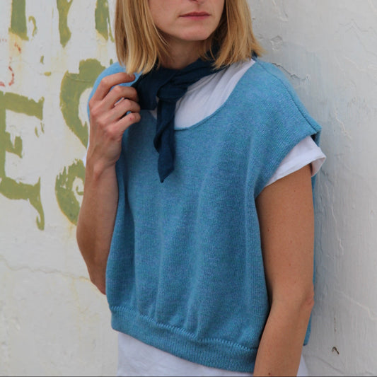 Woman wearing a blue vest over a white shirt with a blurred background