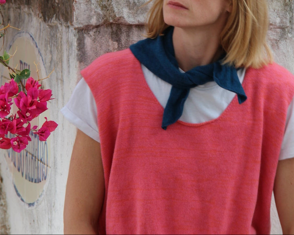 Woman in a red dress with a blue bow standing next to pink flowers.