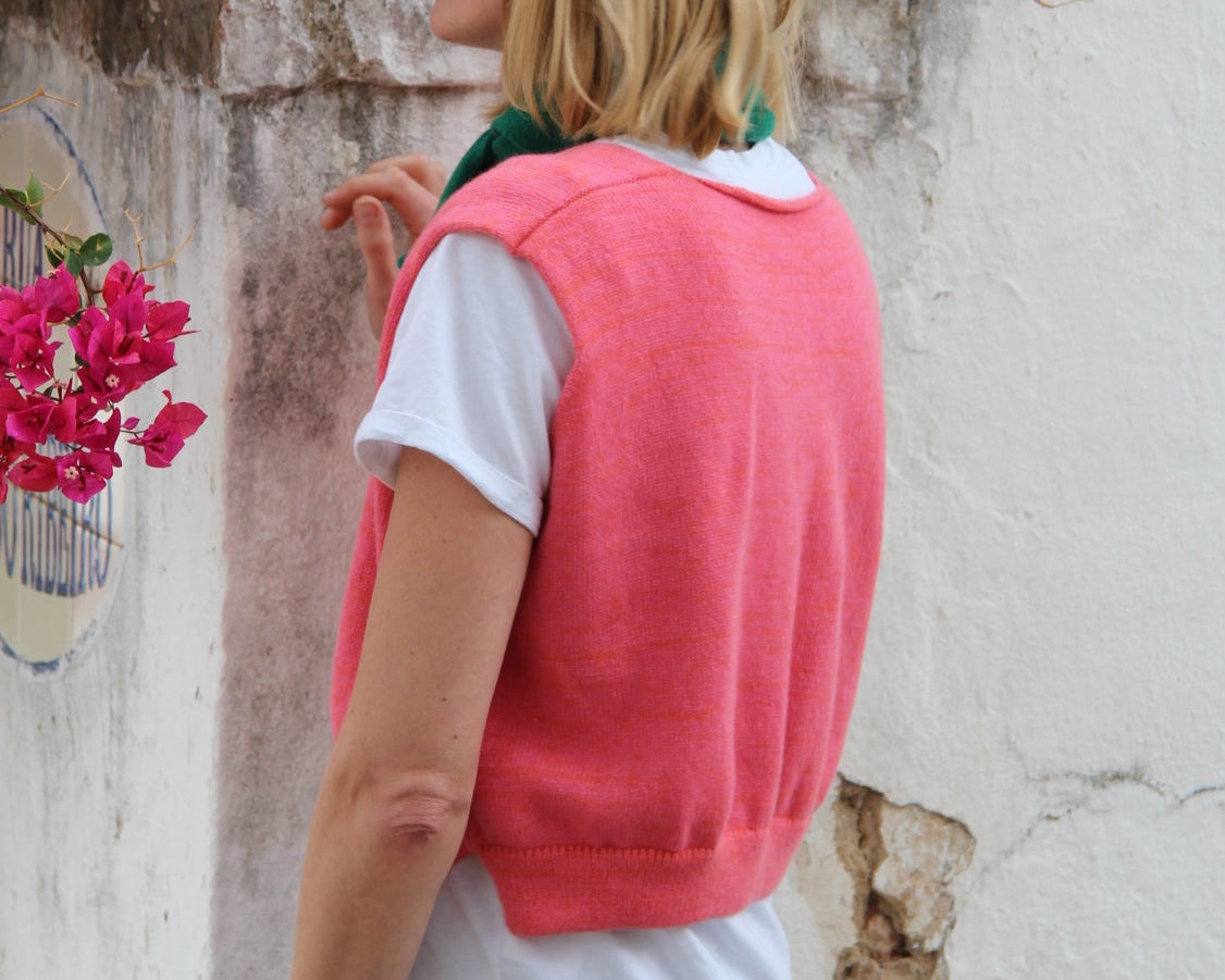 Person wearing a pink jacket and white shirt standing next to a stone wall with pink flowers.