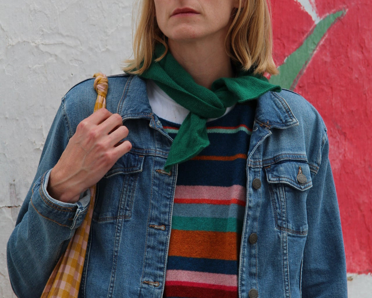 Person wearing a denim jacket over a colorful striped shirt with a abstract painting in the background