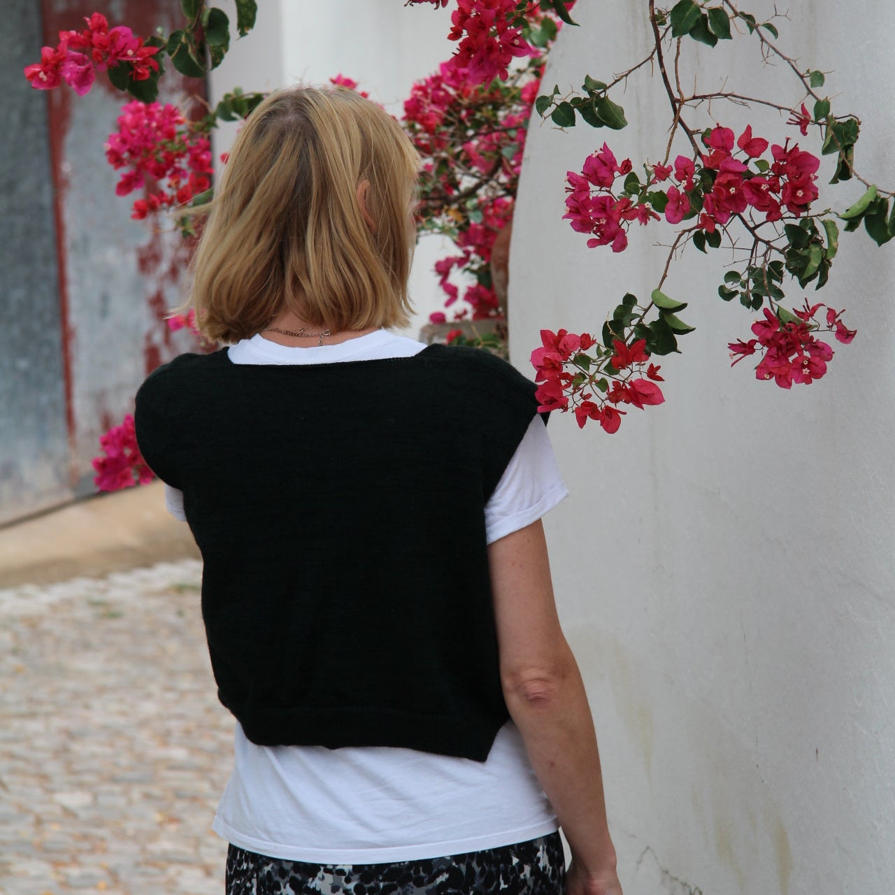 Person in formal attire standing next to a bush with pink flowers on a marble floor.